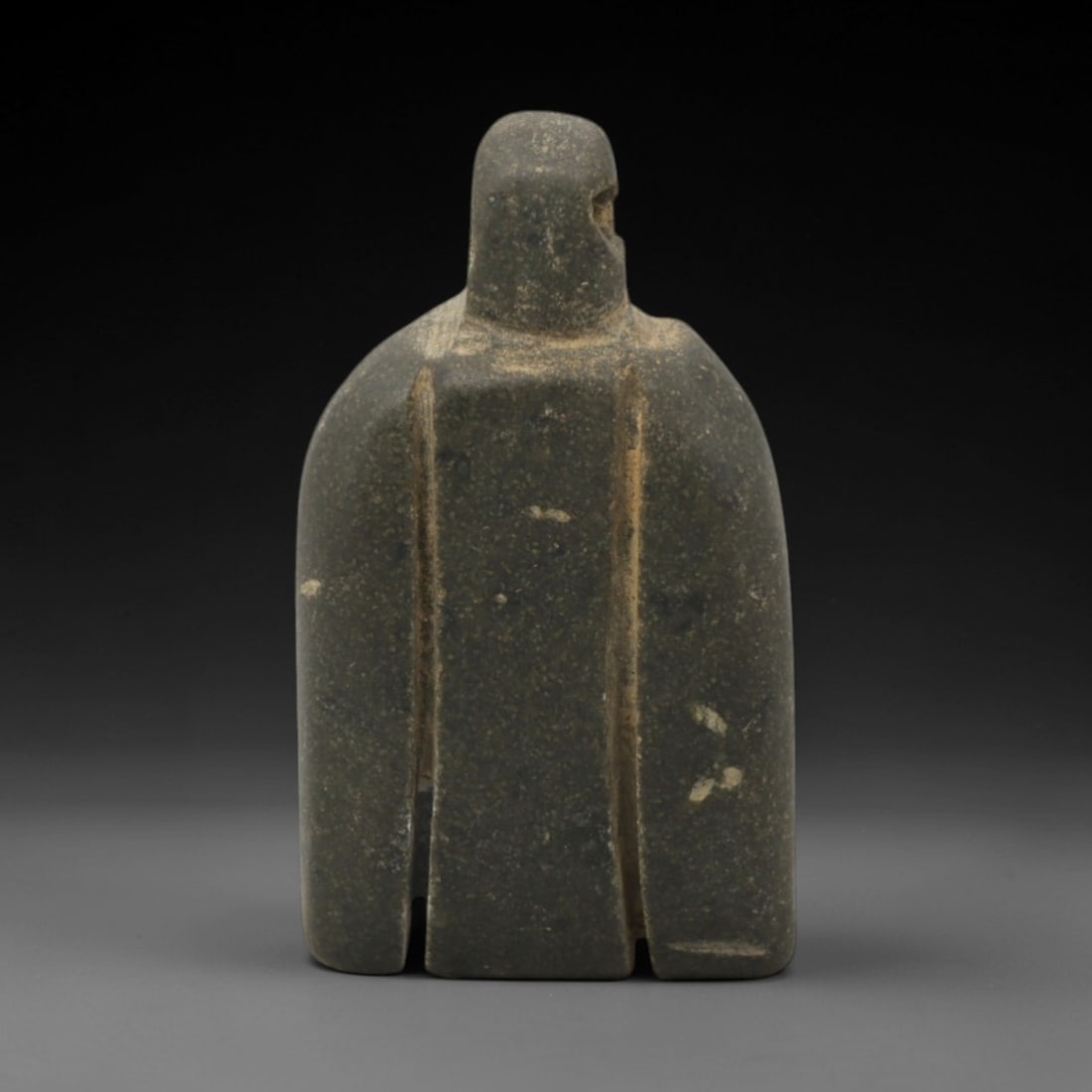 Ancient Stone Idol - Near Eastern Anthropomorphic Figurine, 44XR: Carved from dark grey stone, this miniature anthropomorphic idol features a stylized form with a rounded head, broad cape-like torso, and three vertical lower sections, with a small perforation at the