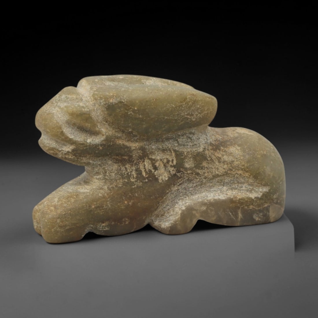 Ancient Stone Zoomorphic Figure - Near Eastern Amulet, 40XQ: Carved from a compact grey-green stone, this amulet takes the form of a recumbent zoomorphic creature, likely a feline or feline-headed deity, with distinct facial detailing and a rounded body. The ca
