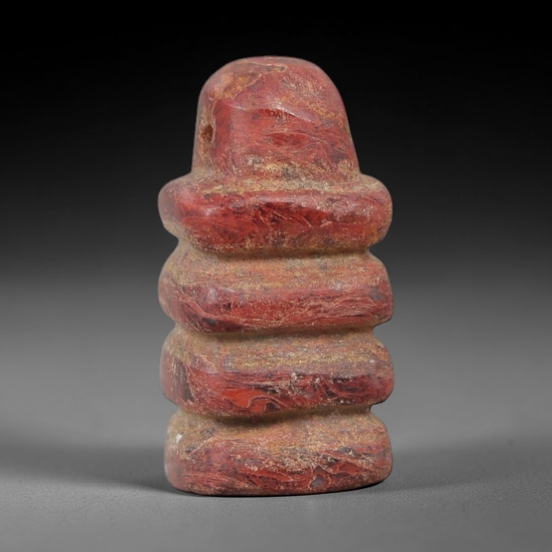 Ancient Stone Djed Amulet - Egyptian Ritual Figurine, 39AG: This amulet is carved from a single piece of deep red stone, exhibiting a fine-grained texture with subtle ochre patina and natural mineral veining across its surface. The form is a stylized Djed pill