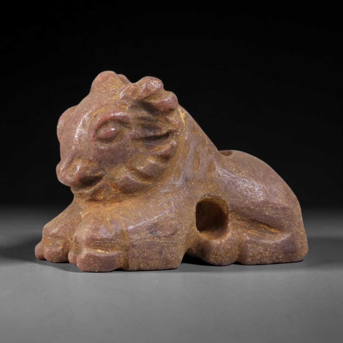 Ancient Stone Ram - Near Eastern Zoomorphic Amulet, 32AS: This zoomorphic amulet is carved from a dense brownish-red stone, displaying a matte, earthy patina consistent with ancient Near Eastern burial contexts. The form depicts a recumbent ram, rendered in