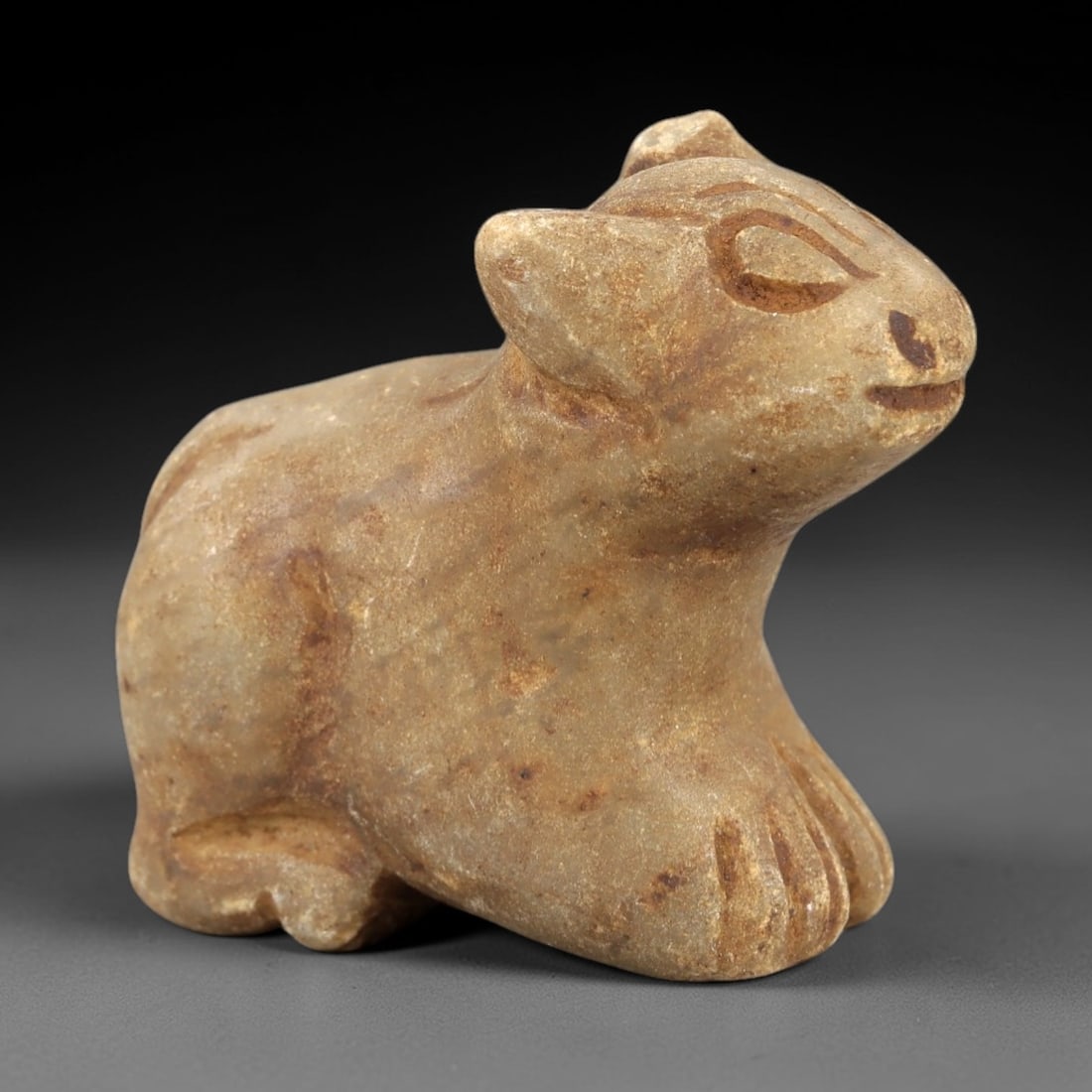 Ancient Stone Feline Amulet - Egyptian Figurine, 88AL: Carved from tan speckled stone, this amulet depicts a crouching feline, likely a cat or lion cub, with stylized incised facial features including almond-shaped eyes, a small nose, and a gently curved