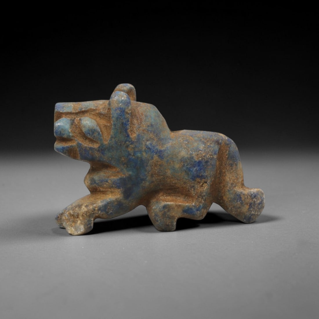 Ancient Lapis Lazuli Feline - Near Eastern Amulet Figurine, 7XT: Carved from lapis lazuli, this amulet depicts a striding feline in a dynamic, angular form. The head is stylized with prominent incised eyes, a defined snout, and upright ears, while the body is rende
