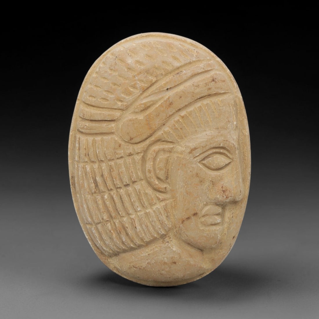 Ancient Stone Bust - Near Eastern Amulet Relief, 32WJ: Carved from stone, this ancient Near Eastern amulet features an oval-shaped bust relief depicting a stylized human head with refined facial features, including a defined eye, lips, and intricately car