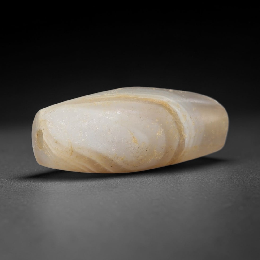 Ancient Banded Agate Bead - Silk Road Indus Valley Bicone Bead: Carved from banded agate, the bead is fashioned in a slender bicone form, with a central drilled perforation for suspension. The stone exhibits delicate, flowing natural banding in creamy white and wa