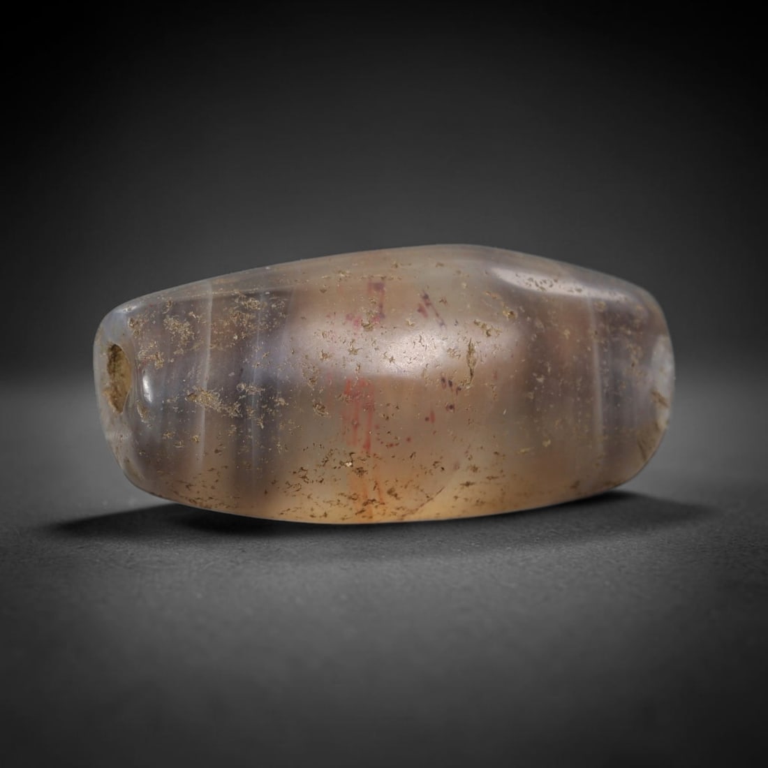 Ancient Agate Bead - Silk Road Artifact: This artifact is crafted from translucent banded agate, shaped into an elongated barrel form with subtle grey and amber banding and faint red mineral striations. The bead features a central perforatio