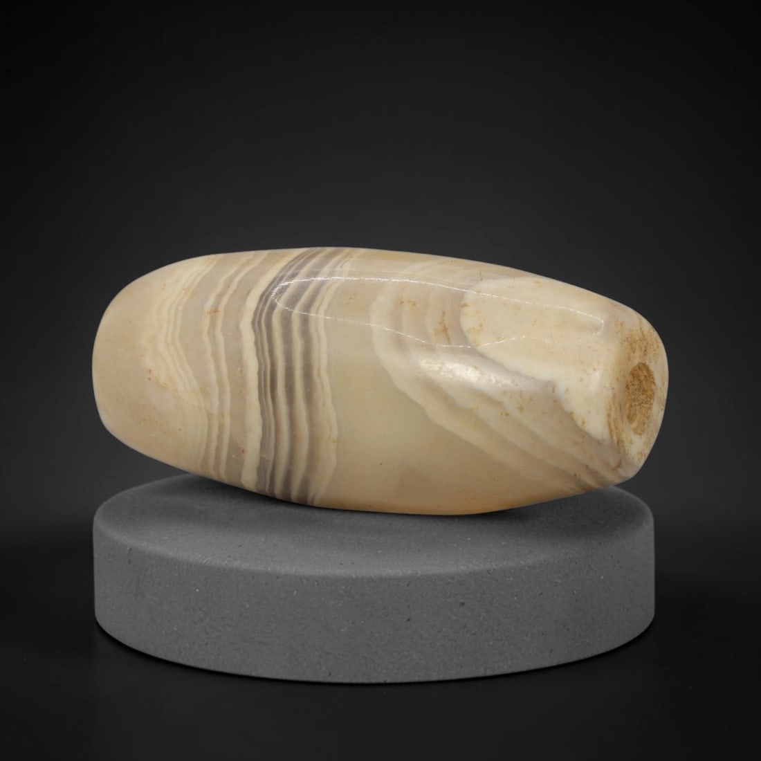 Ancient Agate Bead - Indus Valley Banded: This artifact is crafted from banded agate, exhibiting fine, layered concentric banding in creamy white, warm beige, and muted grey tones across its polished surface. The bead is formed in a smooth ba