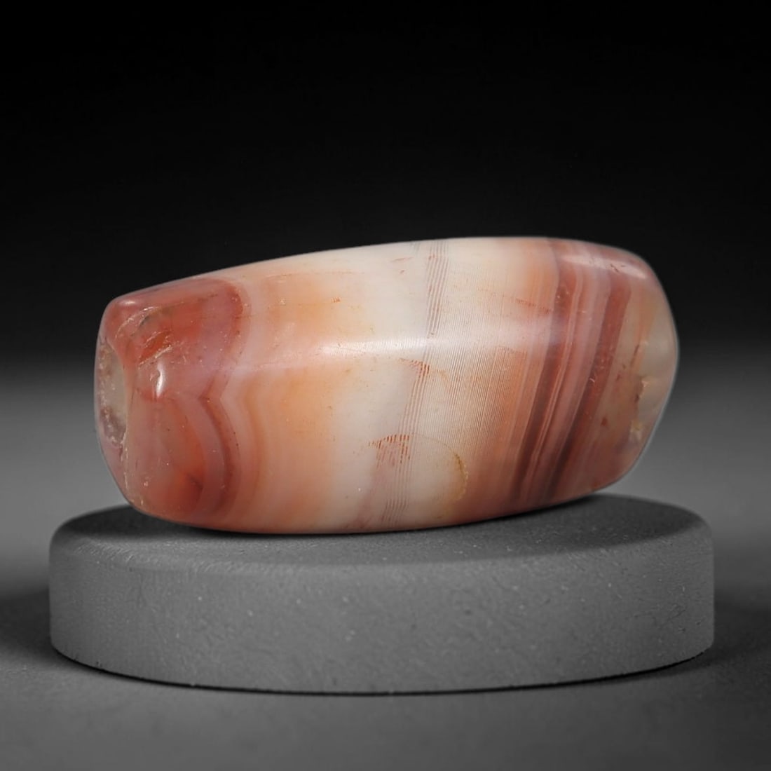 Ancient Banded Agate Bead - Silk Road Artifact: This artifact is crafted from natural banded agate, shaped into a smooth, elongated barrel form with striking concentric red and cream banding. The bead features a central perforation for suspension,