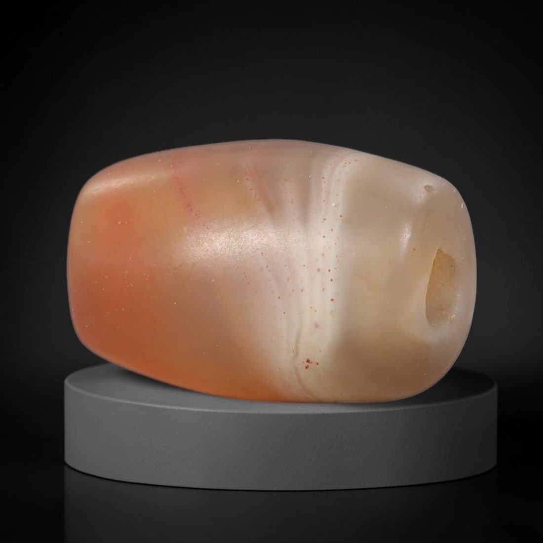 Ancient Agate Bead - Indus Valley Artifact: This artifact is crafted from translucent banded agate, shaped into a compact barrel form with warm peach and cream natural banding. The bead features a central perforation for suspension, consistent