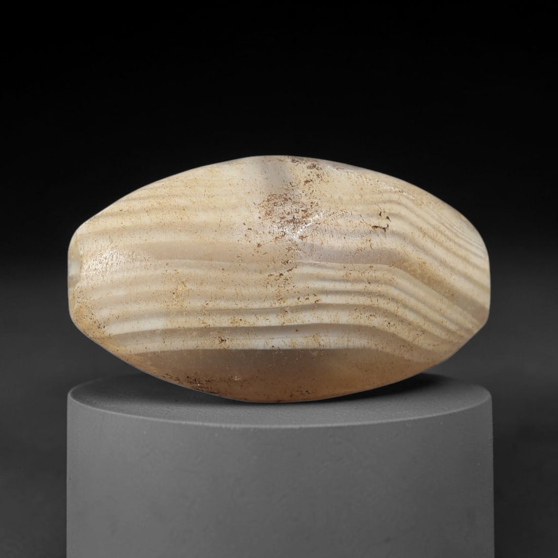 Ancient Agate Bead - Silk Road Bicone Amulet, 37BC: Carved from banded agate, the bead features a smooth symmetrical bicone (double-pointed) form with a polished surface that highlights the stone's striking parallel wavy concentric banding, ranging fro