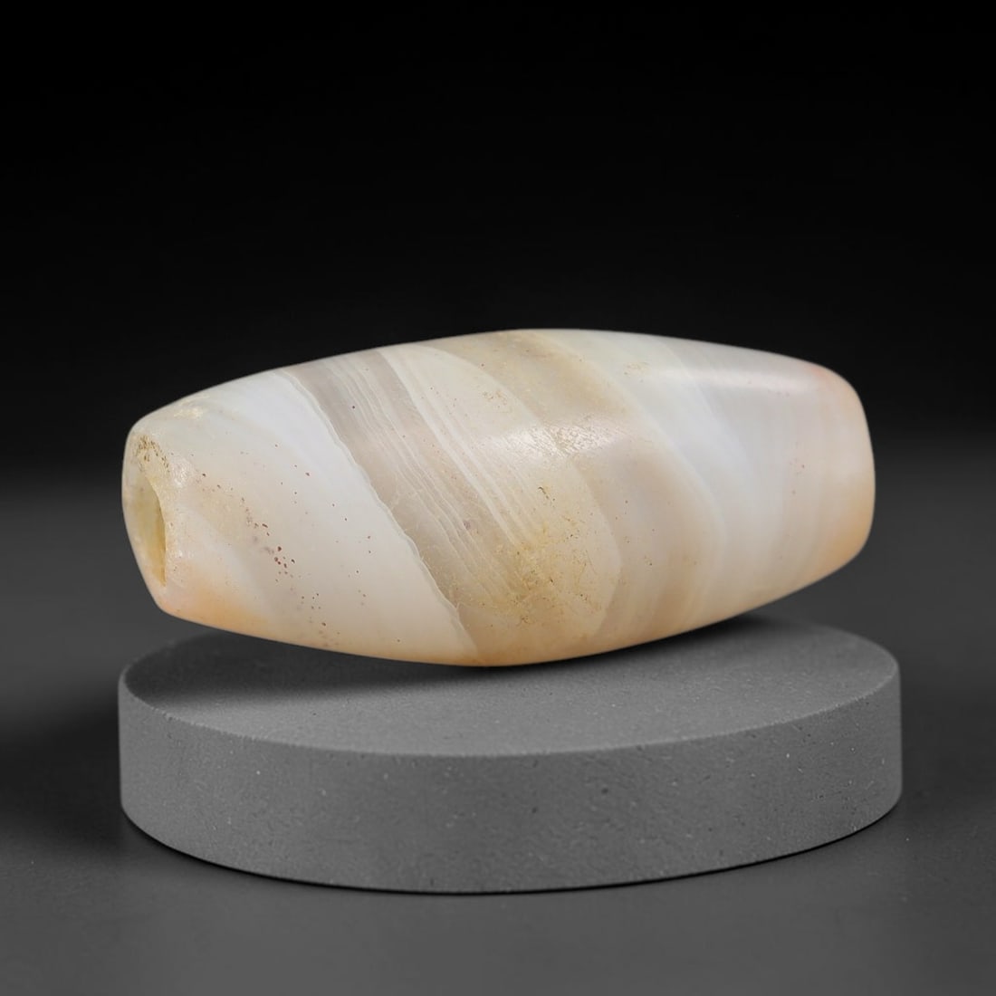 Ancient Agate Bead - Silk Road Bicone Amulet: Carved from banded agate, the bead exhibits an elongated bicone form with a smooth, polished surface that highlights the stone's natural diagonal concentric banding, ranging from translucent milky whi