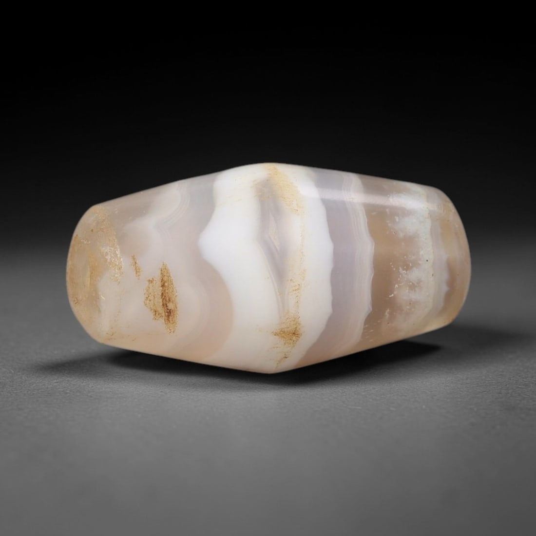 Ancient Agate Bead - Indus Valley Silk Road Barrel Bead: Carved from banded agate, the bead is fashioned in a compact barrel form, with a central drilled perforation for suspension. The stone exhibits natural banding in creamy white, pale beige, and soft am