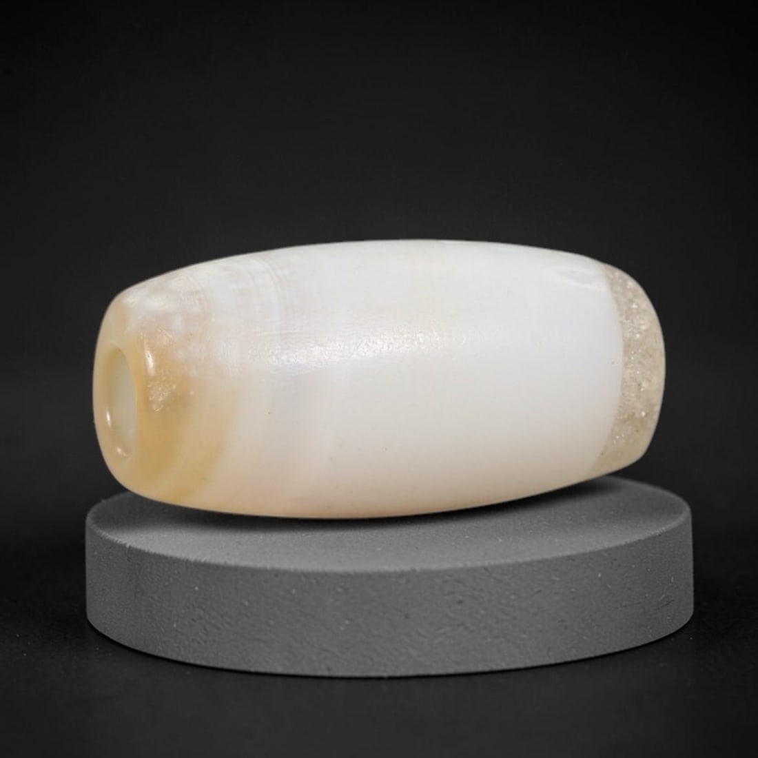 Ancient Agate Bead - Indus Valley Artifact: This artifact is crafted from creamy banded agate, shaped into a smooth, elongated barrel form with subtle natural banding at the terminal ends. The bead features a central perforation for suspension,