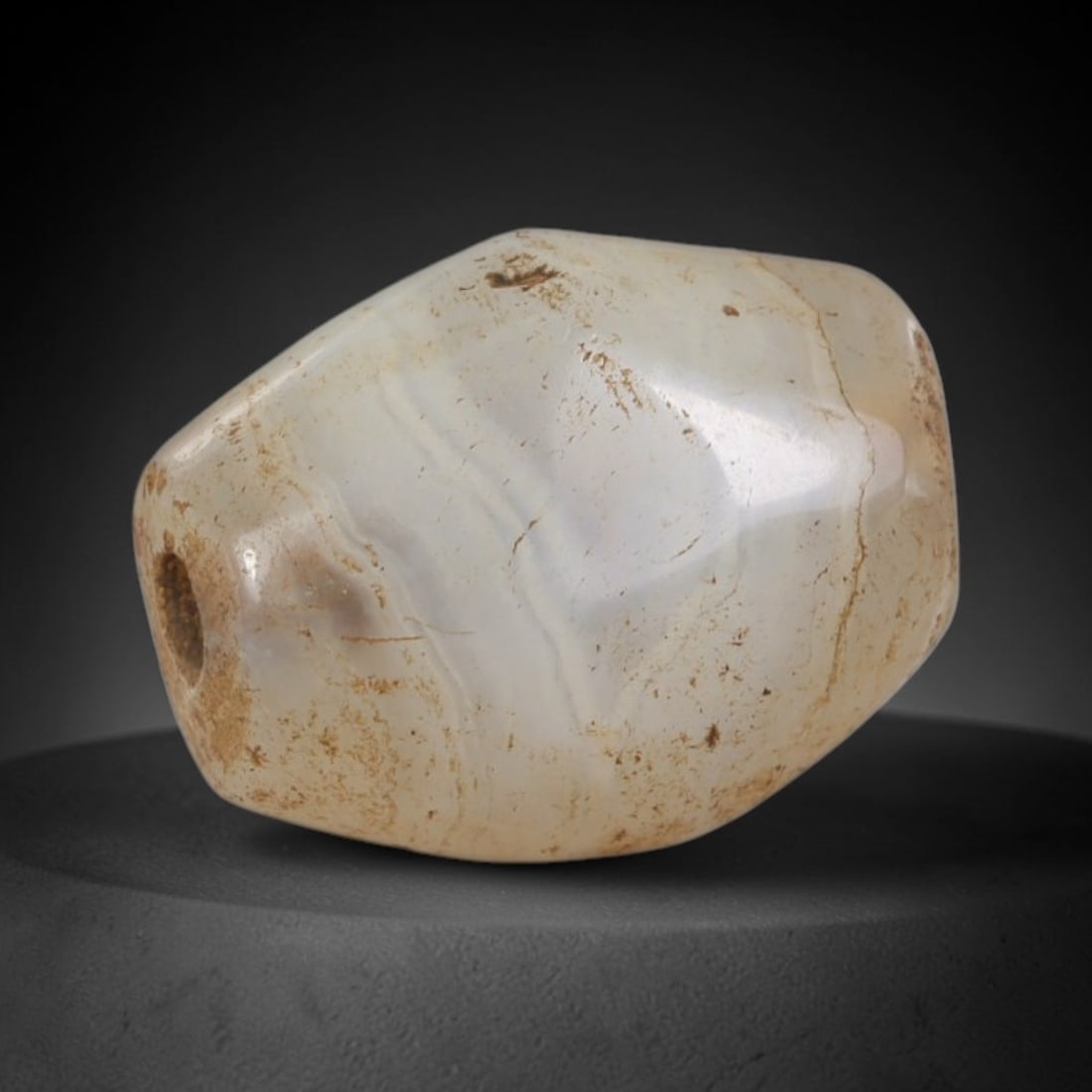 Ancient Agate Bead - Silk Road Miniature: Carved from banded agate, the bead is fashioned in a faceted barrel form with a central perforation for suspension. The stone displays natural, subtle concentric banding in creamy white and translucen
