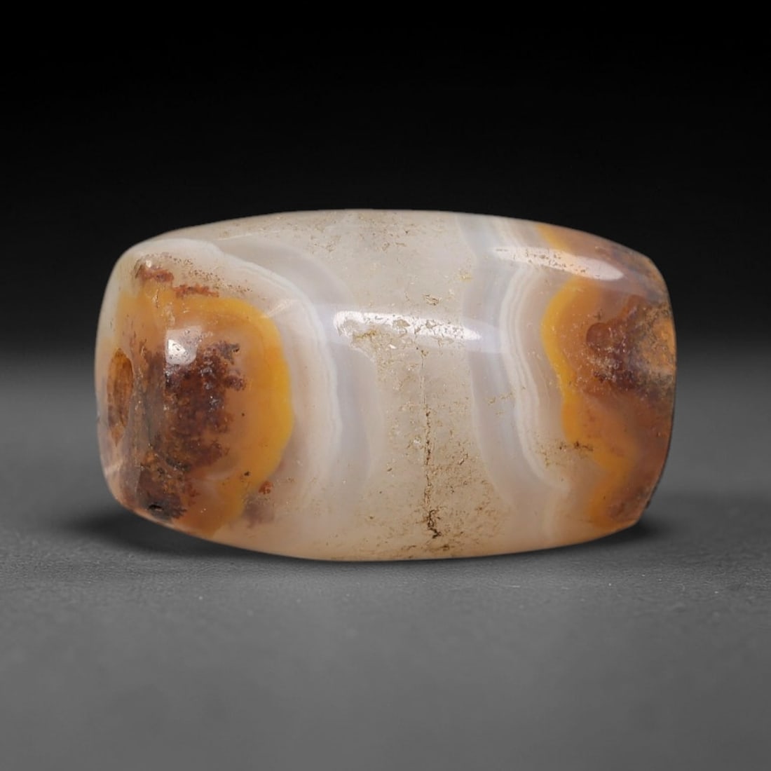 Ancient Banded Agate Bead - Silk Road Indus Valley Barrel Bead: Carved from banded agate, the bead is fashioned in a compact barrel form, with a central drilled perforation for suspension. The stone exhibits striking natural banding in creamy white, warm golden-ye