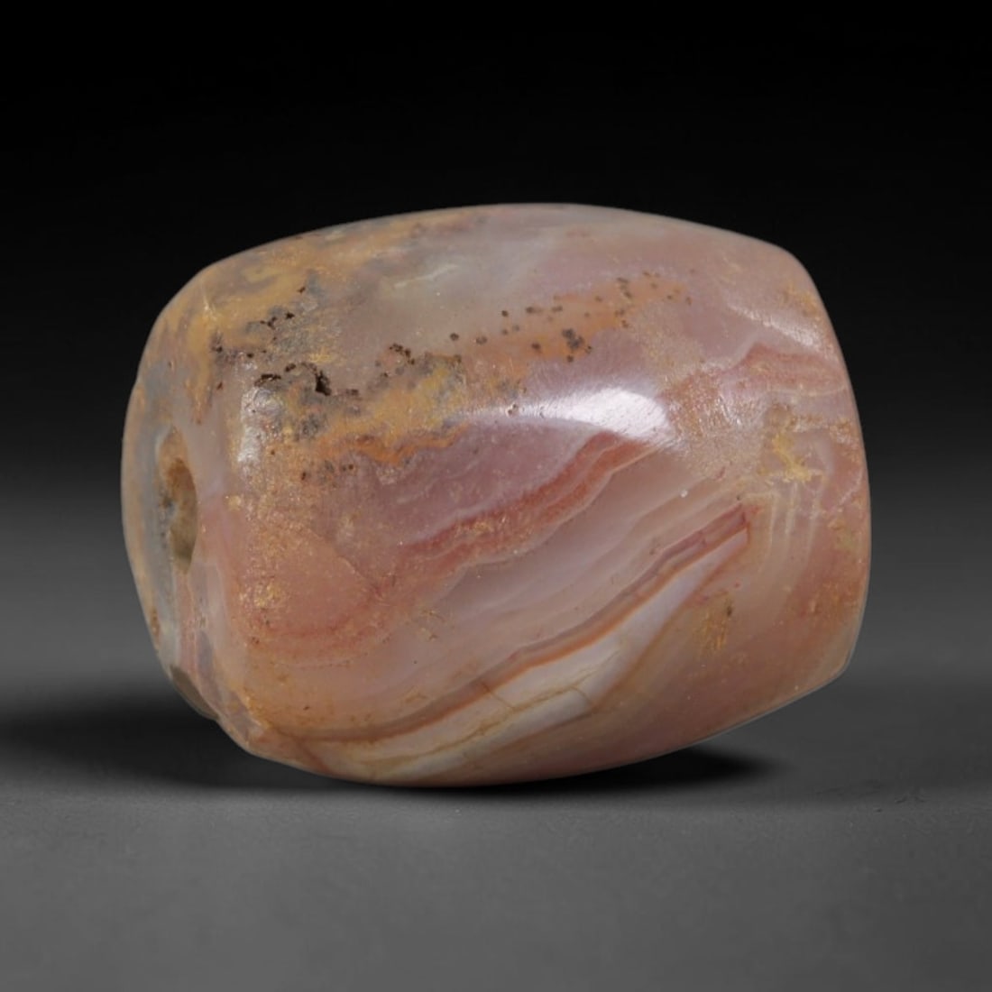 Ancient Agate Bead - Silk Road Bactrian, 100AS: Carved from banded agate, the bead is fashioned in a faceted barrel form with a central perforation for suspension. The stone displays natural, flowing concentric banding in soft pinkish-beige, transl
