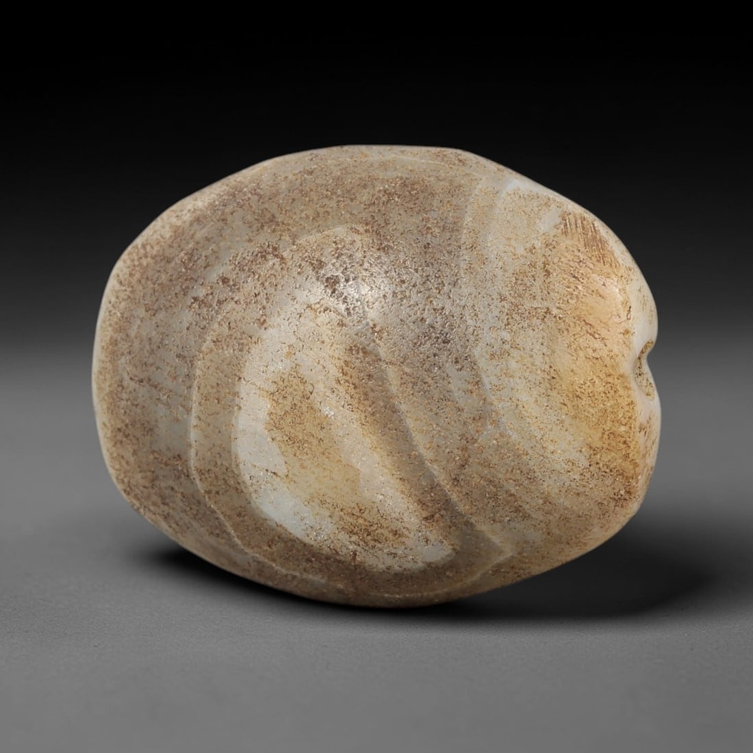Ancient Agate Bead - Bactrian Amulet, 90BC: This artifact is fashioned from banded agate, showcasing layered hues of pale cream, warm amber, and soft grey with subtle earthy mineral encrustation, shaped into a smooth rounded barrel form through
