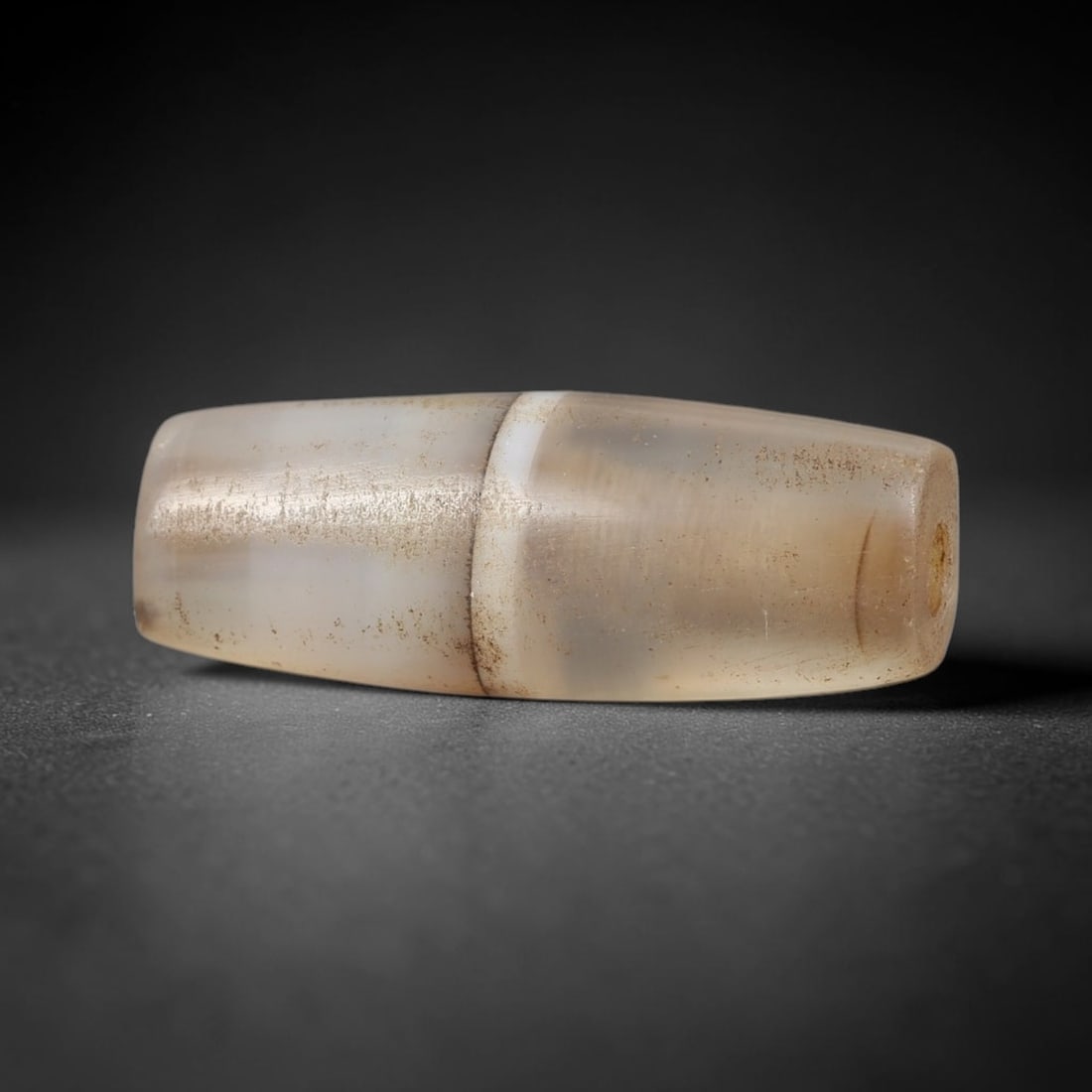 Ancient Agate Bead - Near Eastern Artifact: This artifact is crafted from translucent banded agate, shaped into a segmented barrel form with a distinct central raised ridge dividing the bead into two symmetrical sections. The bead features a ce