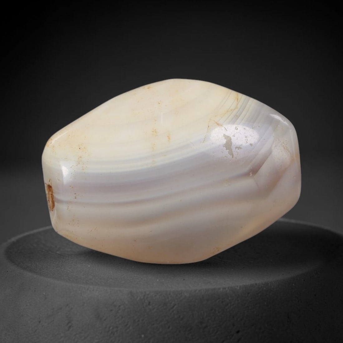 Ancient Agate Bead - Indus Valley Silk Road: Carved from banded agate, the bead is fashioned in a faceted barrel form with a central perforation for suspension. The stone displays natural, flowing concentric banding in creamy white, pale grey, a