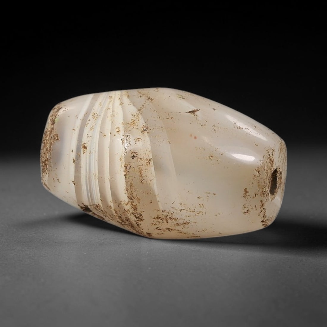 Ancient Agate Bead - Silk Road Ribbed Amulet, 24BC: Carved from translucent banded agate, the bead features a bicone form with a series of finely carved parallel ribbed grooves on one side, showcasing the stone's pale milky white base and subtle intern
