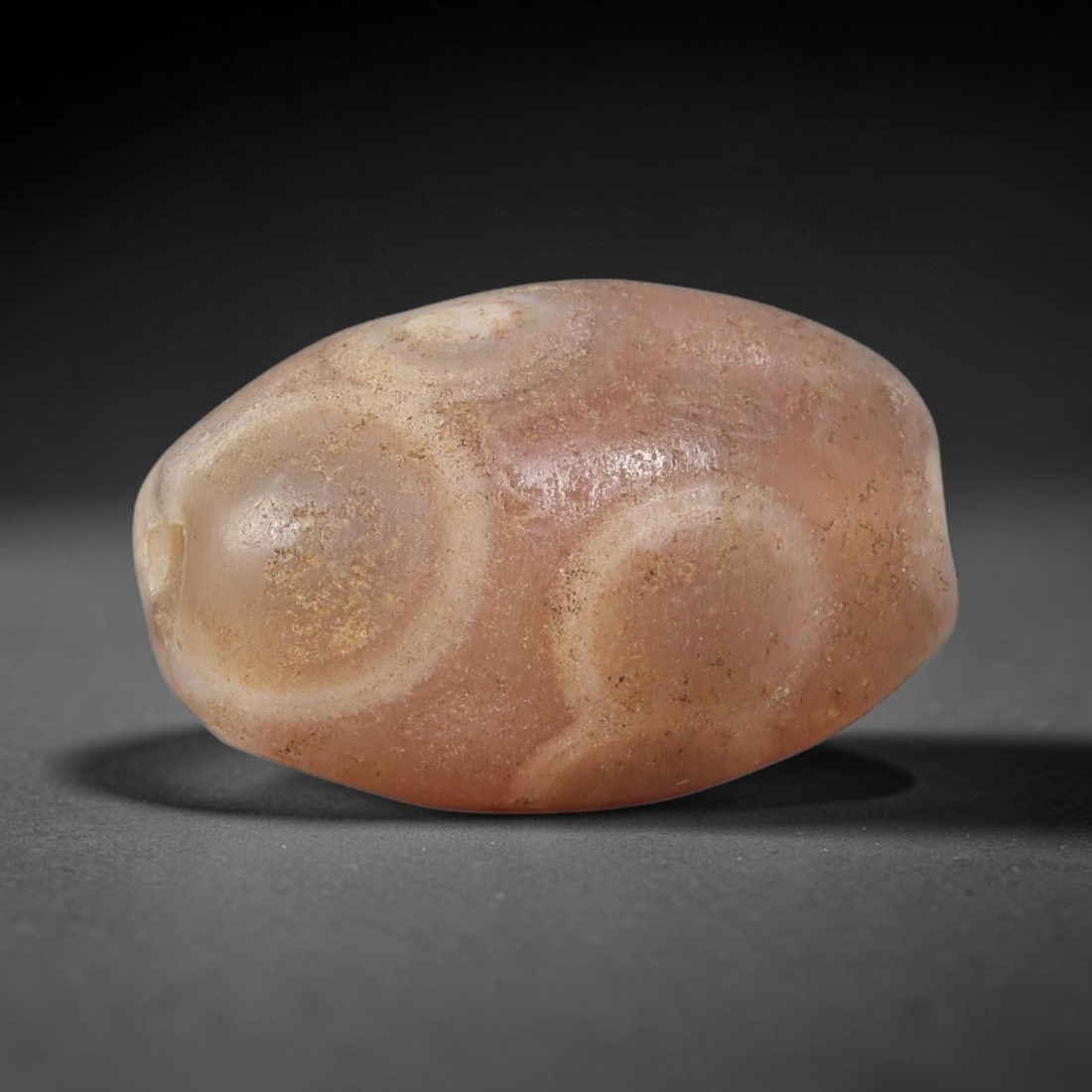 Ancient Eye Agate Bead - Near Eastern Artifact: This artifact is crafted from natural eye agate, shaped into a large rounded oval (barrel) form with a warm peachy-pink base and distinct concentric "eye" banding patterns across the surface. The bead