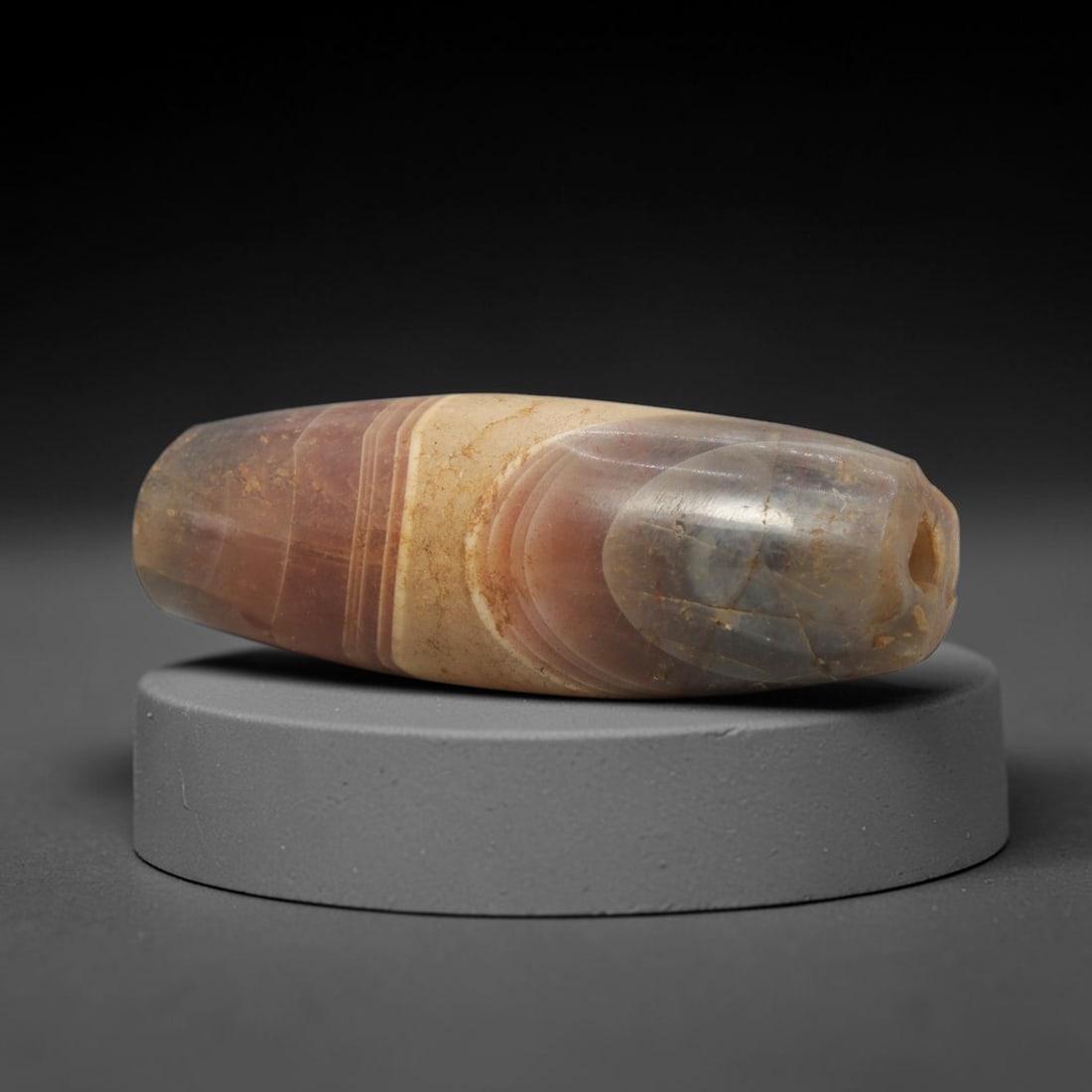 Ancient Agate Bead - Indus Valley Banded Carving: This artifact is crafted from banded agate, exhibiting distinct concentric banding in warm amber, creamy white, and translucent grey tones across its polished, faceted surface. The bead is shaped in a