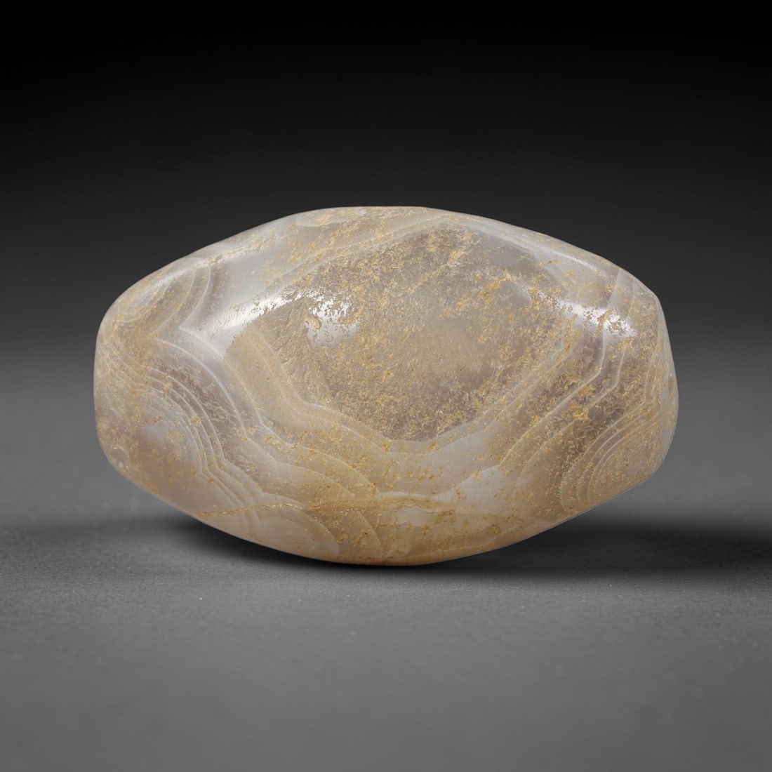 Ancient Banded Agate Bead - Silk Road Western Asiatic Barrel Bead: Carved from banded agate, the bead is crafted into a compact barrel shape with a centered drilled perforation for suspension. The stone features soft, layered banding in creamy off-white and warm ambe