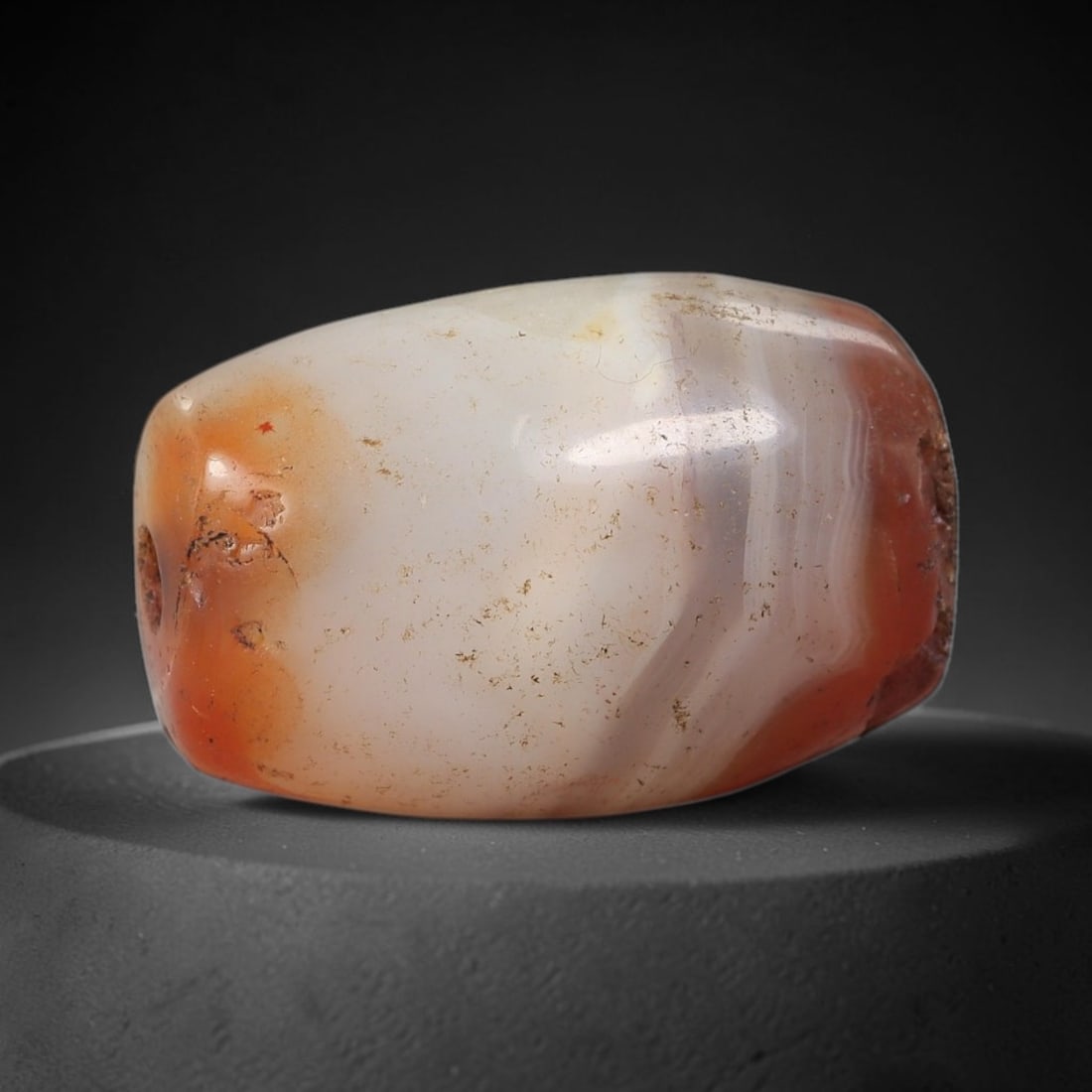 Ancient Carnelian Banded Agate Bead - Indus Valley Artifact: This artifact is crafted from natural carnelian banded agate, shaped into a compact faceted barrel form with a creamy-white central band flanked by rich warm orange-red terminal sections. The bead fea