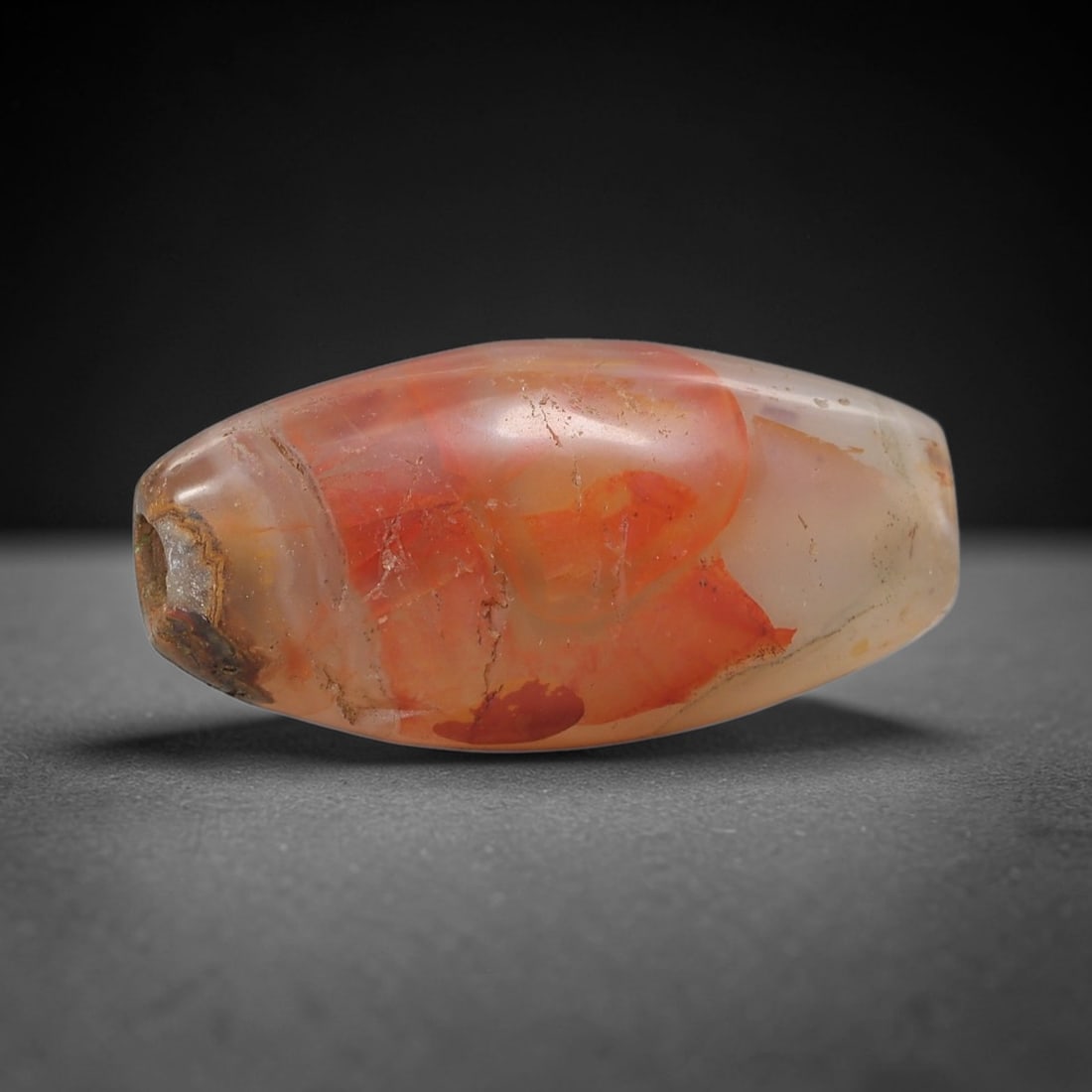 Ancient Carnelian Agate Bead - Silk Road Indus Valley Bead: Carved from translucent banded carnelian agate, the bead is shaped in an elongated barrel form, with a central drilled perforation for suspension. The stone displays striking natural banding in vibran