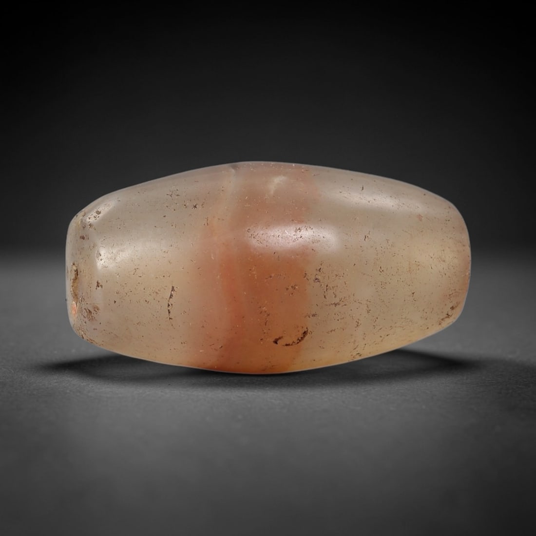 Ancient Carnelian Agate Bead - Silk Road Indus Valley Barrel Bead: Carved from carnelian agate, the bead is fashioned in a compact barrel form, with a central drilled perforation for suspension. The stone exhibits a soft, translucent base in warm honey and blush-pink