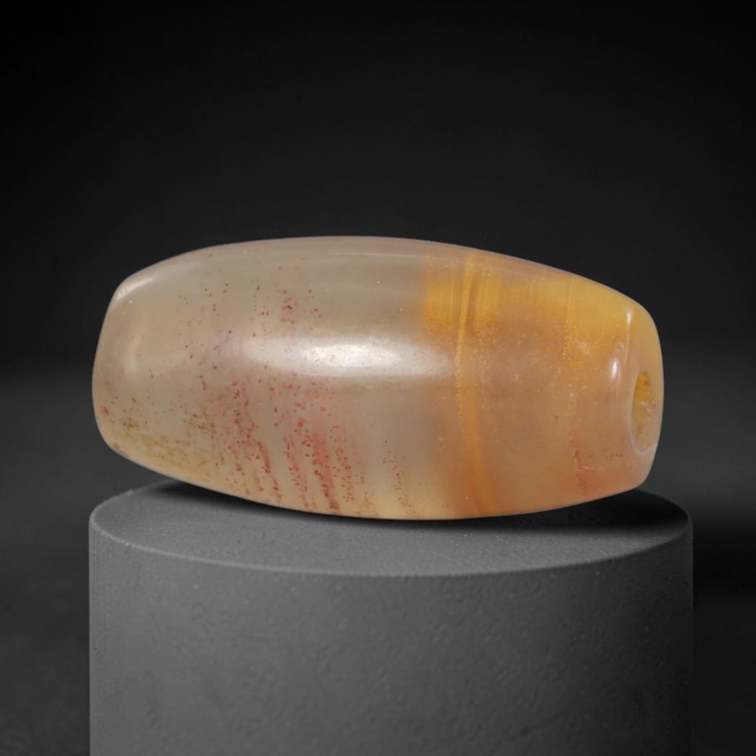 Ancient Agate Bead - Silk Road Western Asiatic: This artifact is fashioned from translucent agate, featuring subtle natural banding in warm amber tones and fine red mineral inclusions scattered across its polished surface. The bead is shaped in an