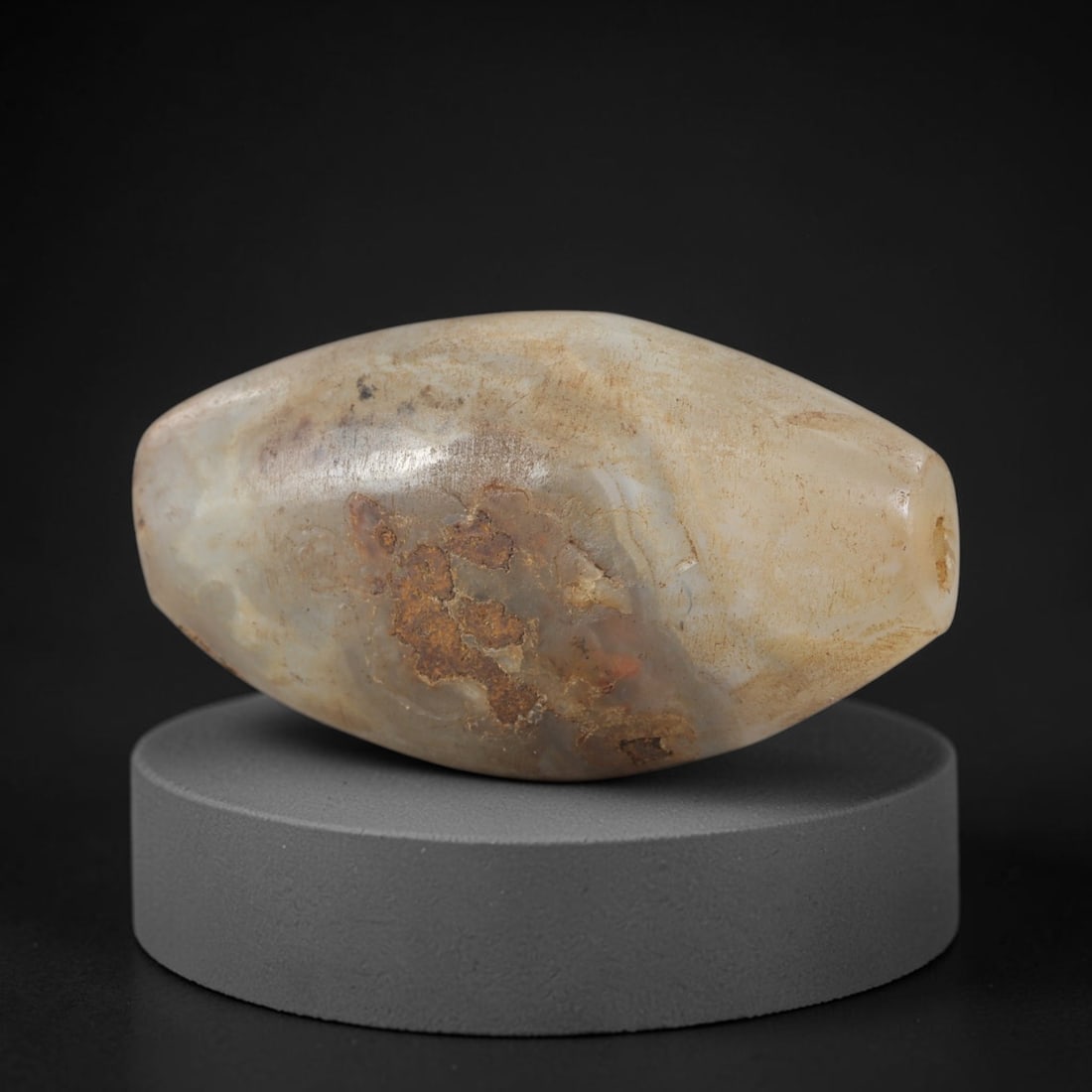 Ancient Agate Bead - Indus Valley Silk Road: Carved from banded agate, the bead is fashioned in a bi-conical barrel form with a central perforation for suspension. The stone displays natural, muted concentric banding in creamy beige, translucent