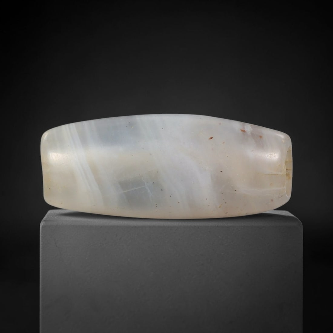 Ancient Agate Bead - Near Eastern Artifact, 70BD: This artifact is crafted from translucent banded agate, shaped into an elongated barrel form with delicate wavy white banding across its surface. The bead features a central perforation for suspension