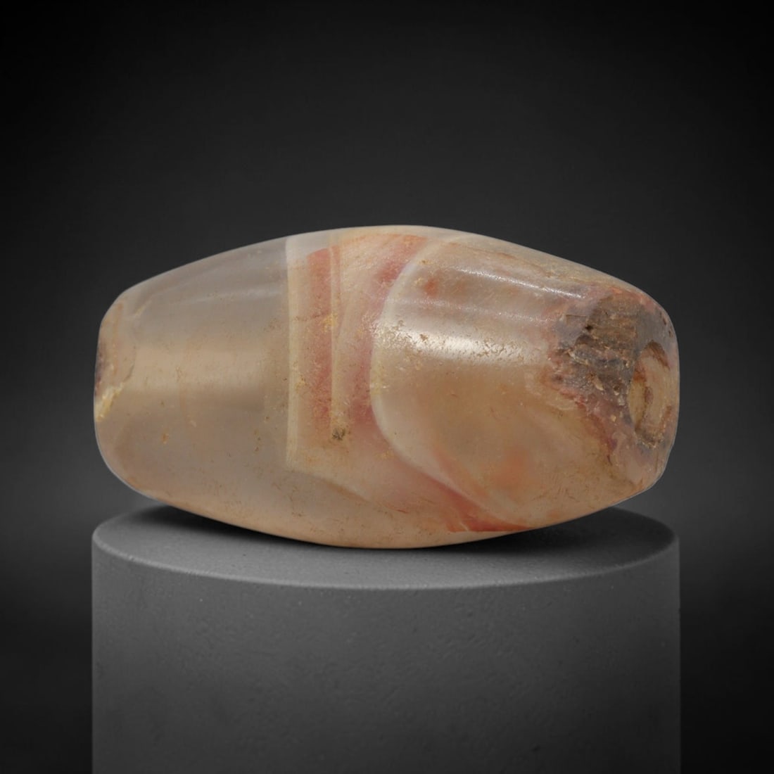Ancient Agate Bead - Indus Valley Banded Carving: This artifact is crafted from banded agate, showcasing striking concentric banding in warm rose-red and creamy translucent tones across its polished, faceted surface. The bead is shaped in a smooth, b