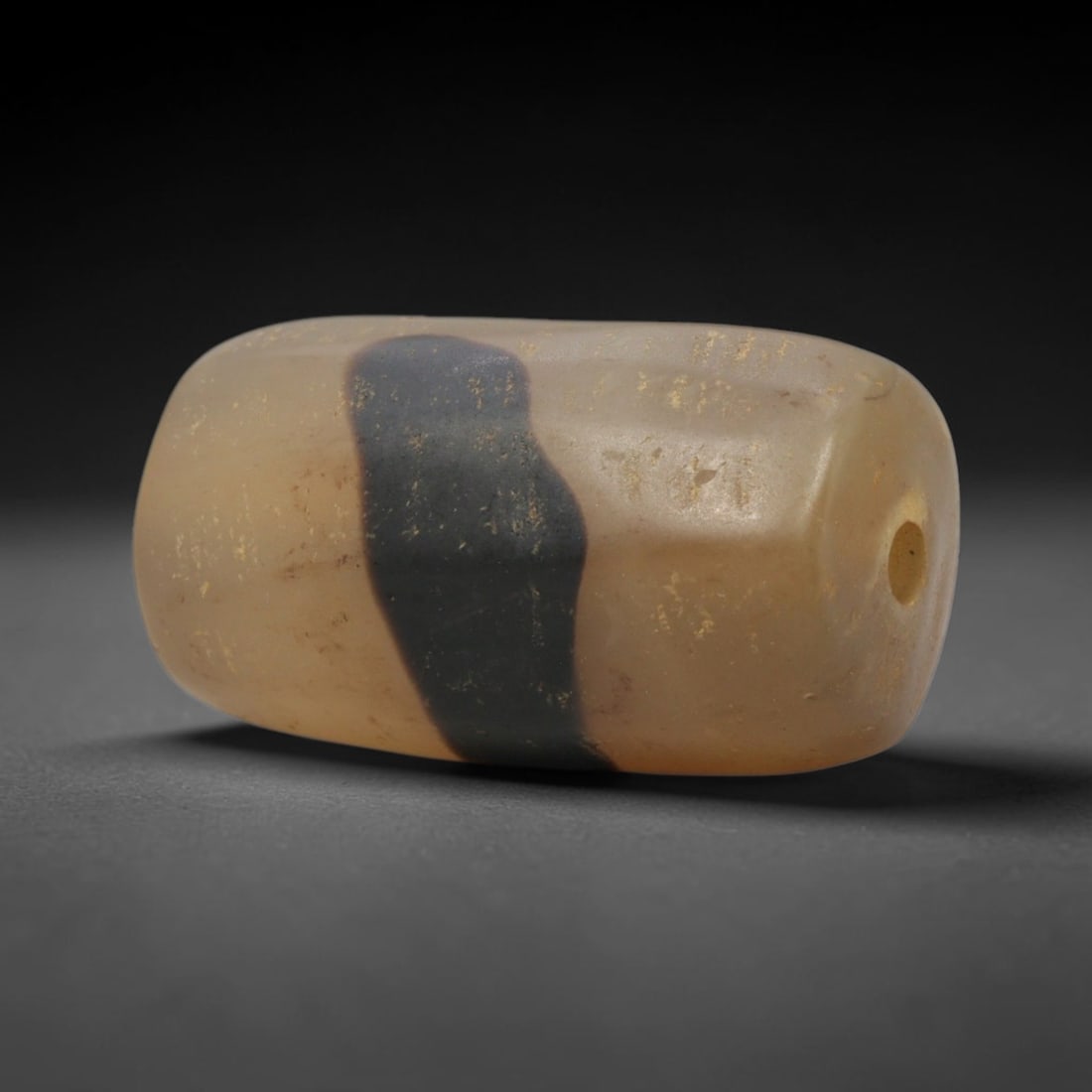 Ancient Agate Bead - Indus Valley Banded: This artifact is crafted from banded agate, featuring a bold, striking band of deep black set against a warm, creamy translucent base across its polished, faceted surface. The bead is formed in a smoo