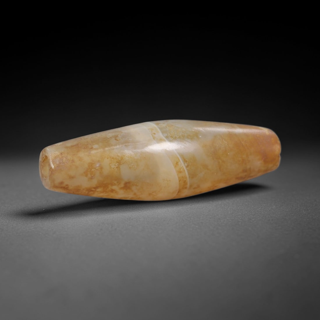 Ancient Agate Bicone Bead - Silk Road Indus Valley Bead: Carved from banded agate, the bead is fashioned in a slender bicone (elongated bullet) form, with a central drilled perforation for suspension. The stone exhibits natural banding in creamy white and w