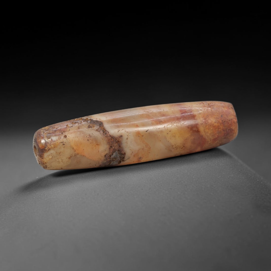 Ancient Agate Bead - Indus Valley Banded Carving: This artifact is crafted from banded agate, showcasing a rich blend of warm honey-amber, deep rust-red, and earthy brown mineral hues with prominent natural crusting and weathering across its polished