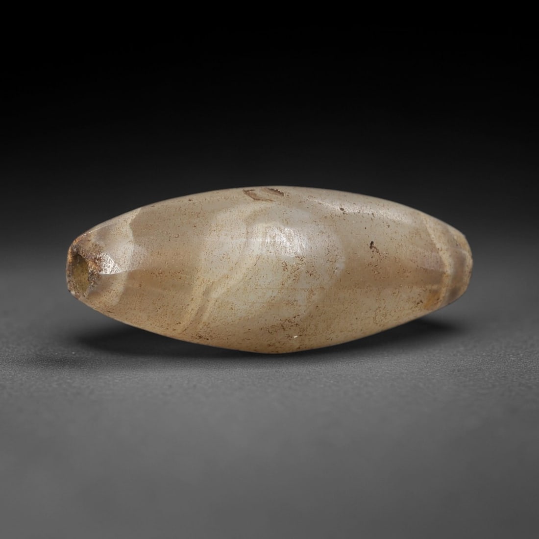 Ancient Agate Bead - Silk Road Indus Valley Bicone Bead: Carved from banded agate, the bead is fashioned in a slender bicone form, with a central drilled perforation for suspension. The stone exhibits subtle natural banding in creamy beige and pale grey ton
