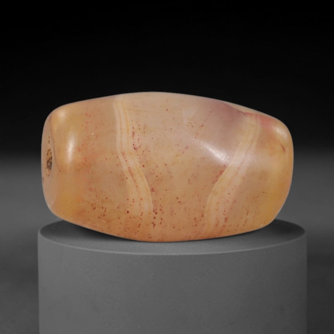Ancient Agate Bead - Indus Valley Banded Carving: This artifact is crafted from translucent banded agate, exhibiting subtle natural banding in warm peach and cream tones, with fine red mineral inclusions scattered across its polished surface. The bea