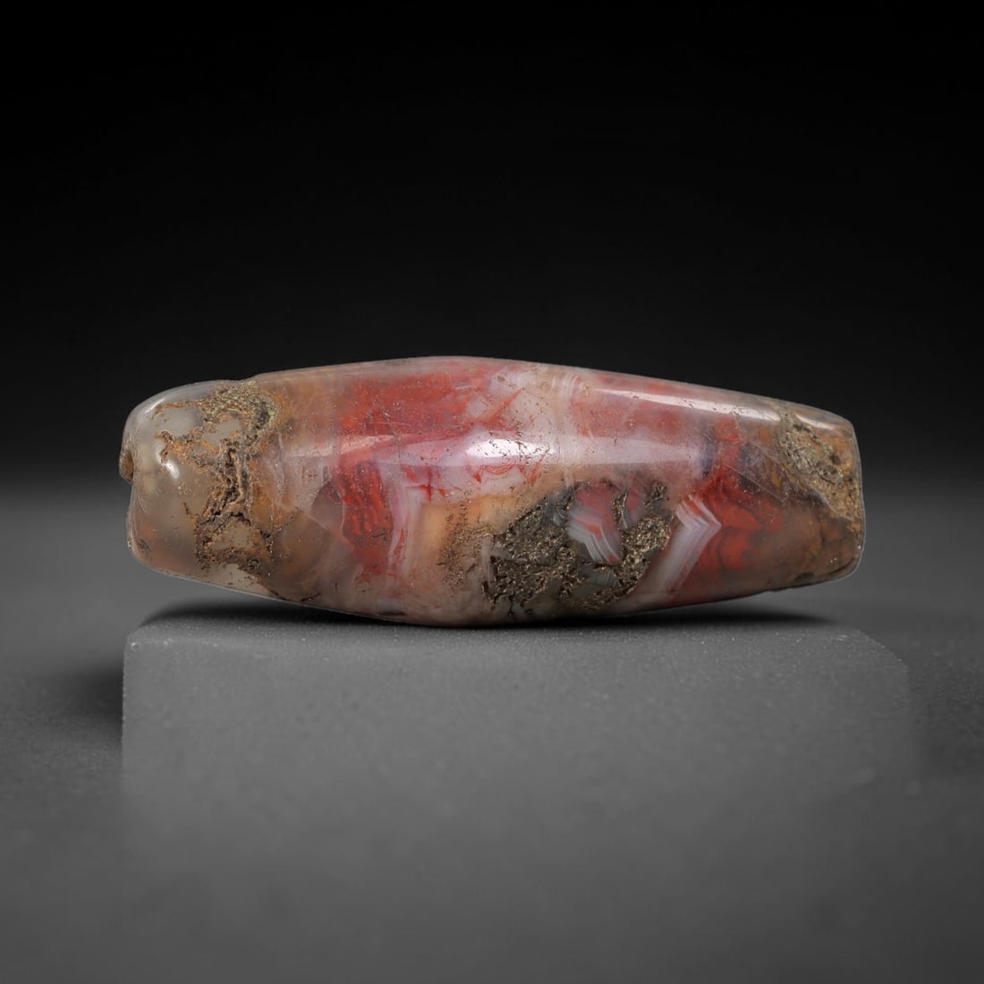 Ancient Agate Bead - Silk Road Bicone Amulet: Carved from banded agate, the bead exhibits a symmetrical bicone form with a smooth, polished surface that highlights the stone's striking red and white banding, alongside natural mineral encrustation