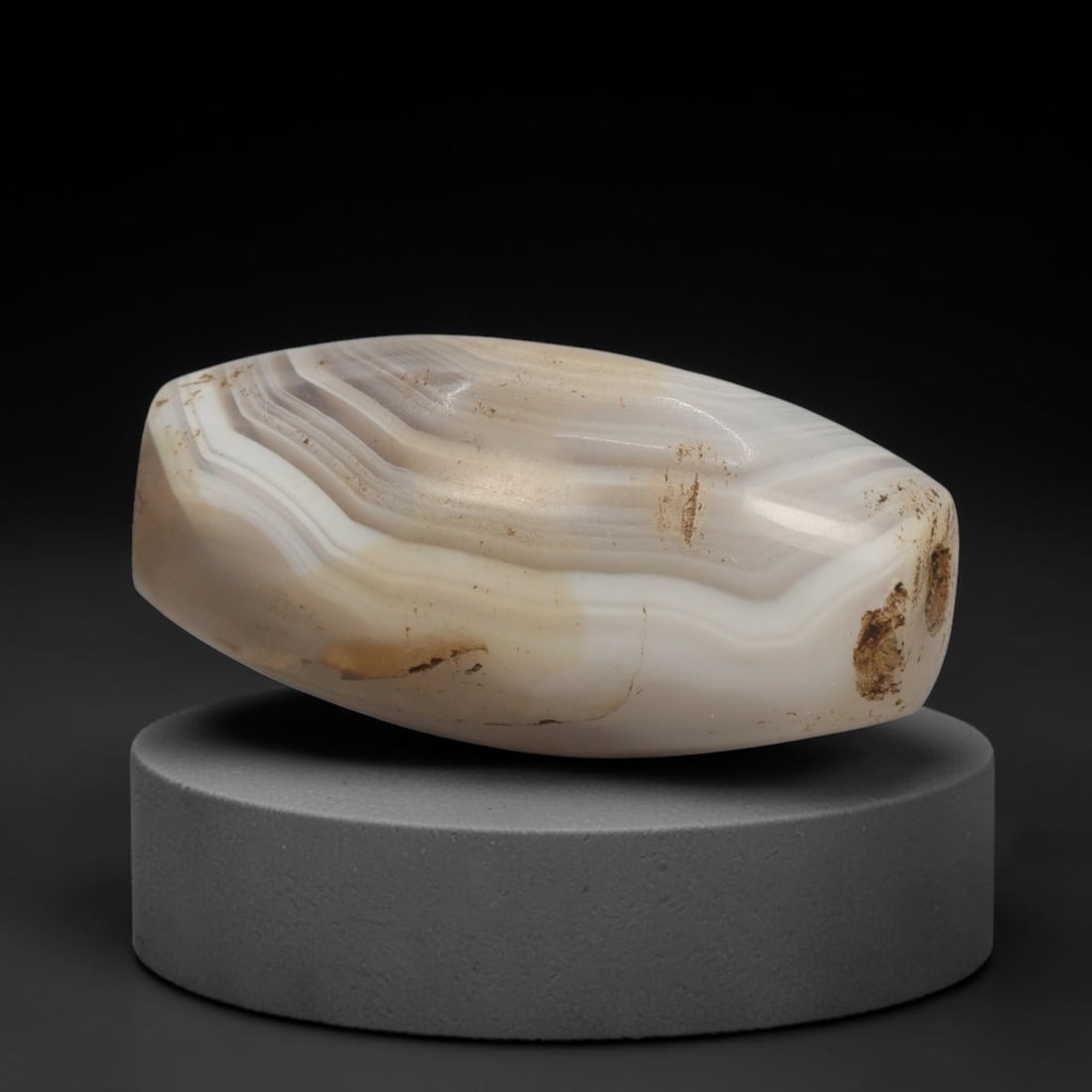 Ancient Agate Bead - Silk Road Bactrian Pendant: This bead is carved from richly banded agate, exhibiting expert lapidary craftsmanship reflective of ancient Bactrian and Silk Road bead artistry. The elongated barrel form features a smooth central p