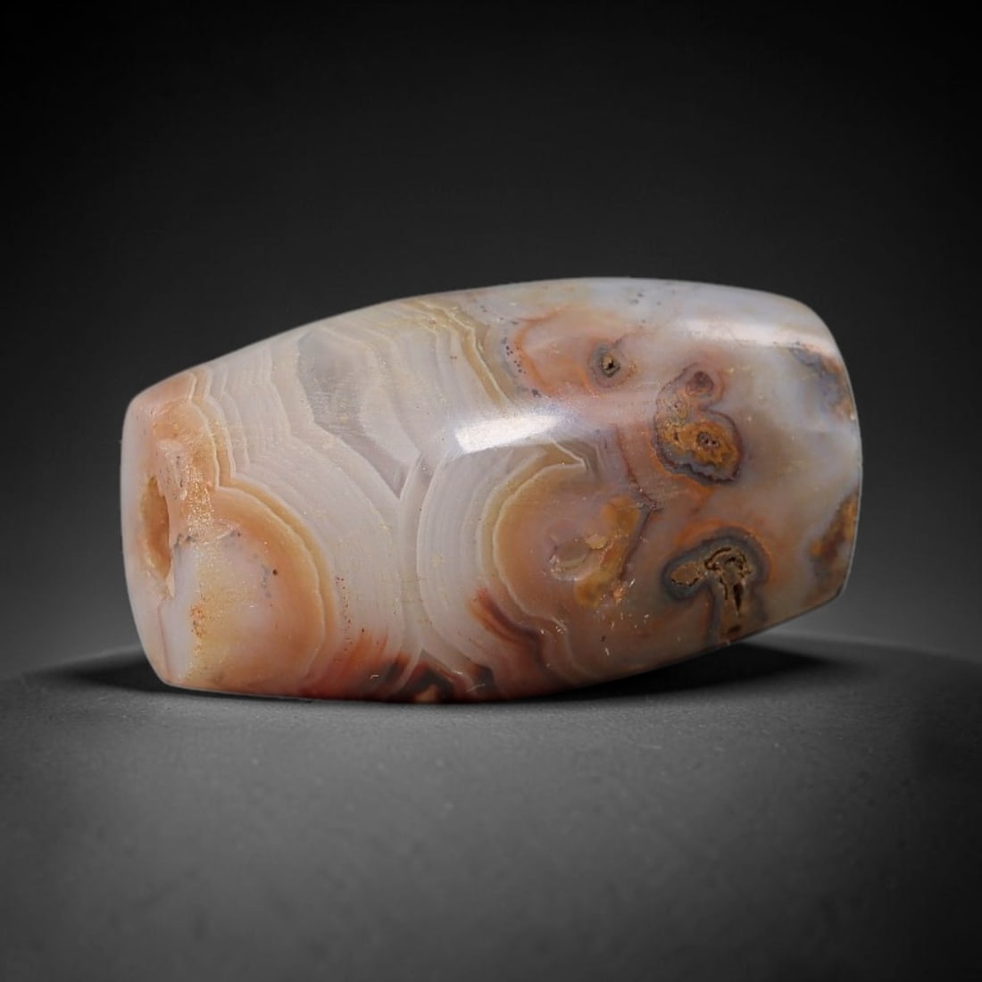 Ancient Banded Agate Bead - Near Eastern Artifact: This artifact is crafted from natural banded agate, shaped into a compact barrel form with intricate concentric banding in warm peach, cream, and rust hues, accented by distinctive eye-like mineral in