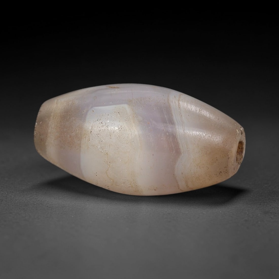 Ancient Agate Bead - Indus Valley Silk Road Barrel Bead: Carved from banded agate, the bead is fashioned in a classic barrel form, with a central drilled perforation for suspension. The stone exhibits natural concentric banding in translucent milky white, p