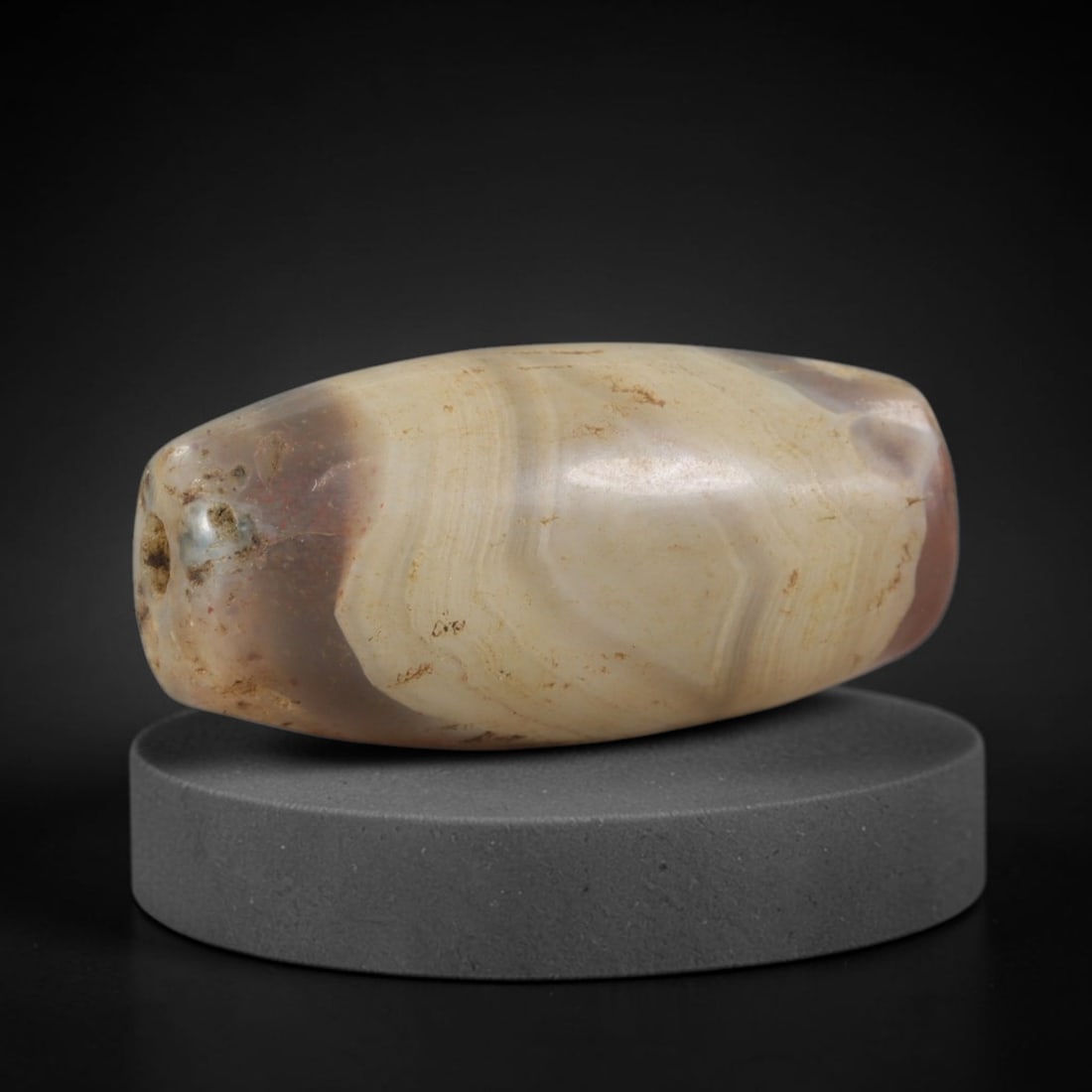 Ancient Agate Bead - Indus Valley Silk Road: Carved from banded agate, the bead is fashioned in a cylindrical, barrel form with a central perforation for suspension. The stone displays natural concentric banding in creamy beige, translucent grey