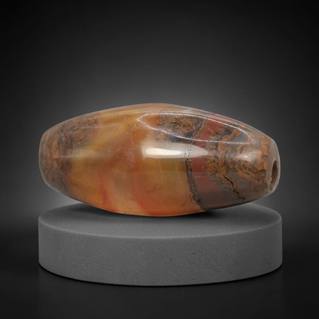Ancient Agate Bead - Indus Valley Banded Carving: This artifact is crafted from banded agate, showcasing a rich blend of warm amber, deep red, and earthy brown mineral hues with striking dendritic and layered banding across its polished surface. The