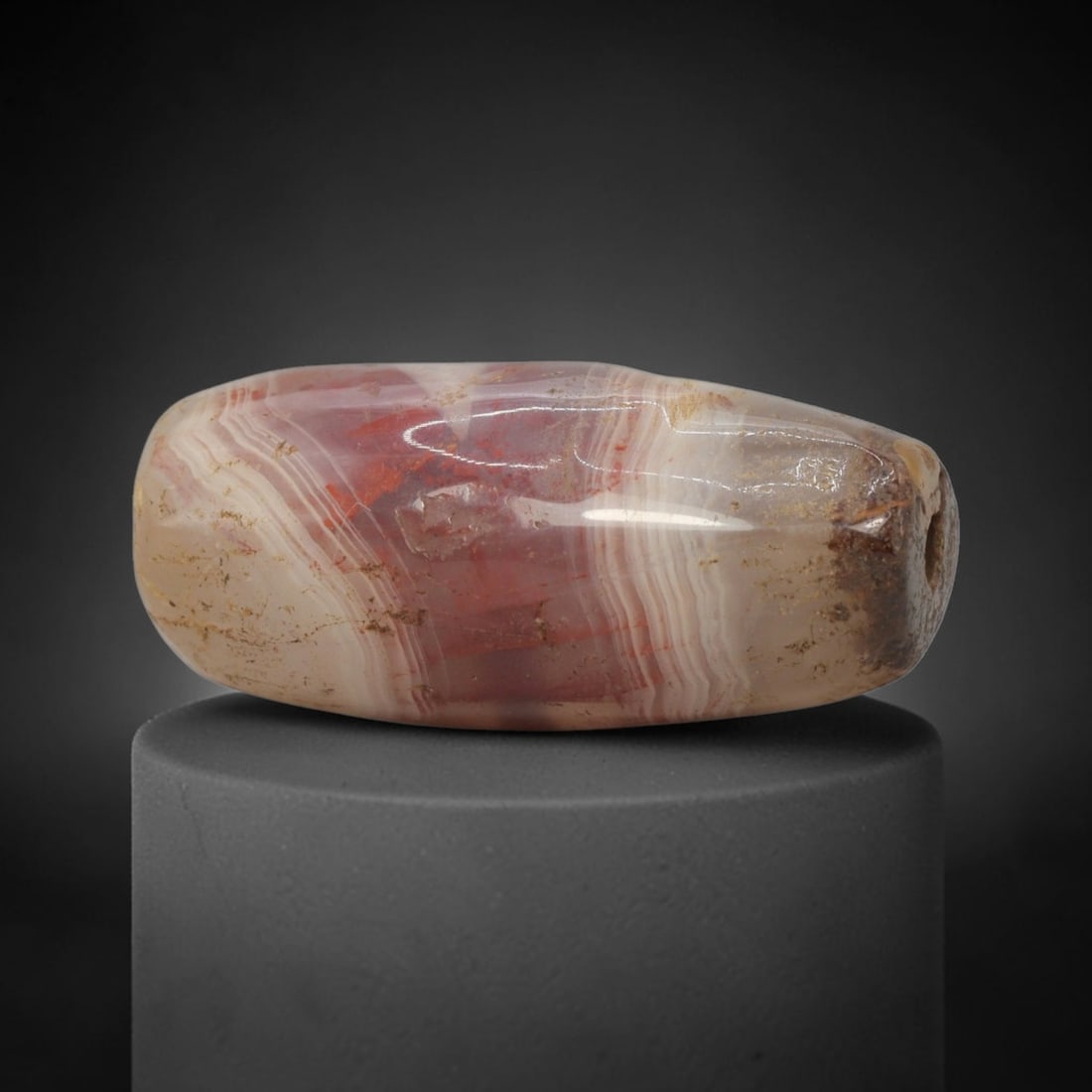 Ancient Agate Bead - Indus Valley Banded Carving: This artifact is crafted from banded agate, showcasing striking concentric banding in rich rose-red, creamy white, and warm amber tones across its polished surface. The bead is shaped in a smooth, bar