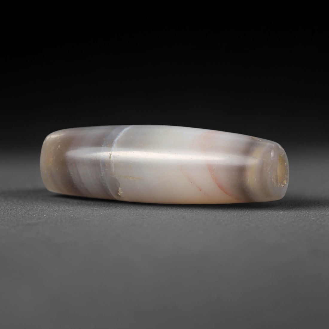Ancient Banded Agate Bead - Large Silk Road Indus Valley Bicone Bead: Carved from banded agate, this bead is fashioned into an exceptionally long, slender bicone form, with a central drilled perforation for suspension. The stone exhibits striking, layered banding in smo