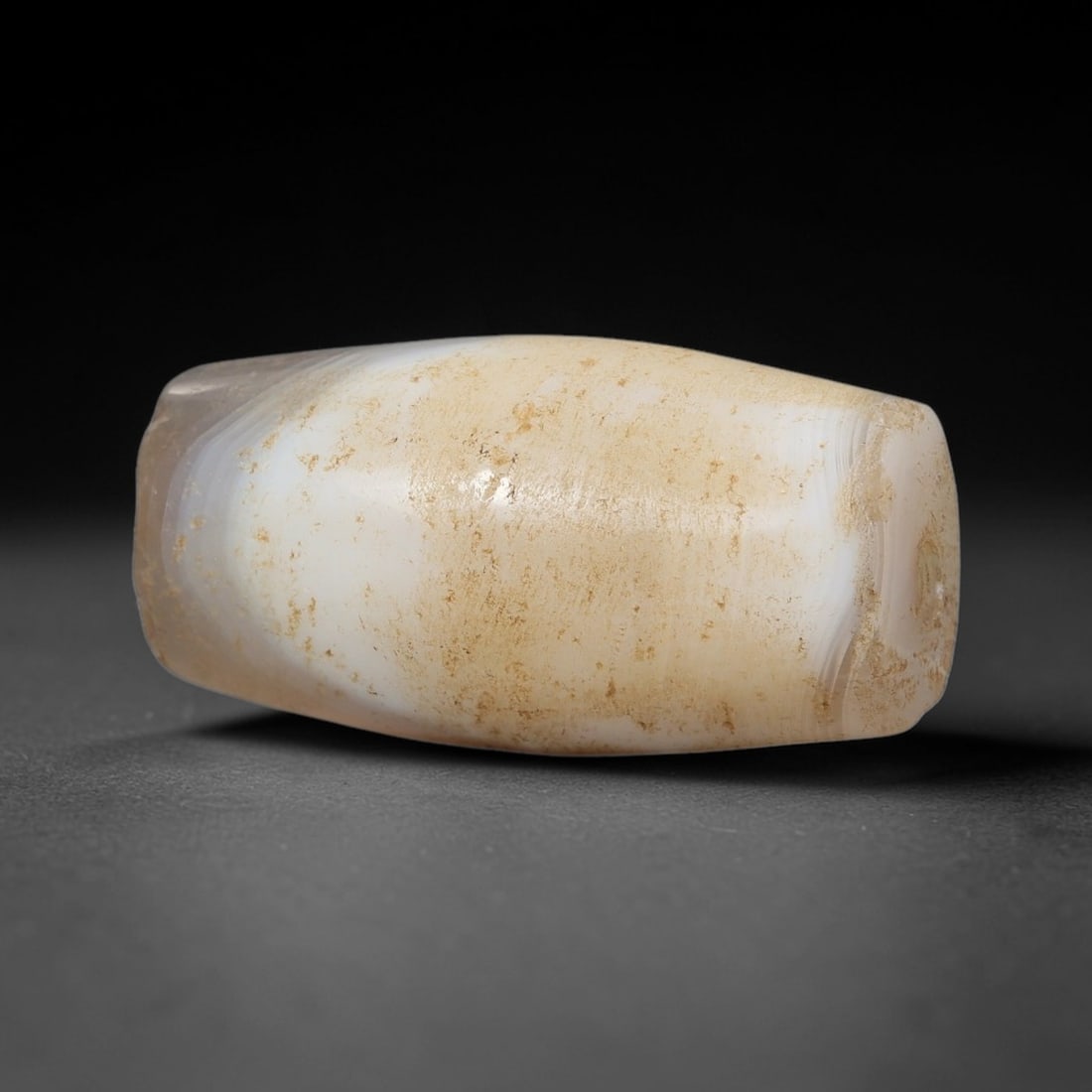 Ancient Milky Agate Bead - Silk Road Indus Valley Barrel Bead: Carved from milky white and pale beige banded agate, the bead is shaped in a compact barrel form, with a central drilled perforation for suspension. The stone exhibits subtle internal banding and incl