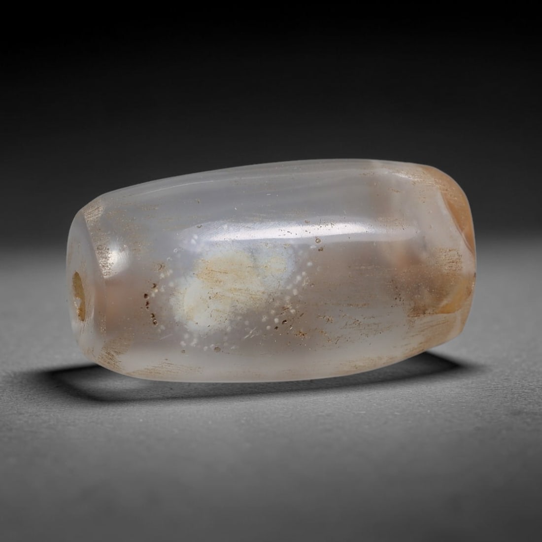 Ancient Agate Bead - Indus Valley Artifact: This artifact is crafted from translucent agate, shaped into an elongated barrel form with distinctive dendritic and milky mineral inclusions across its surface. The bead features a central perforatio