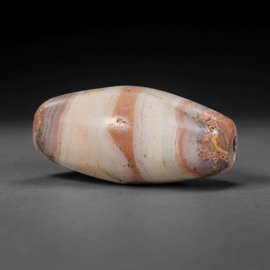 Ancient Agate Barrel Bead - Silk Road Indus Valley Bead: Carved from multicolored banded agate, the bead is shaped in a classic elongated barrel form, with a central drilled perforation for suspension. The stone displays natural concentric banding in creamy
