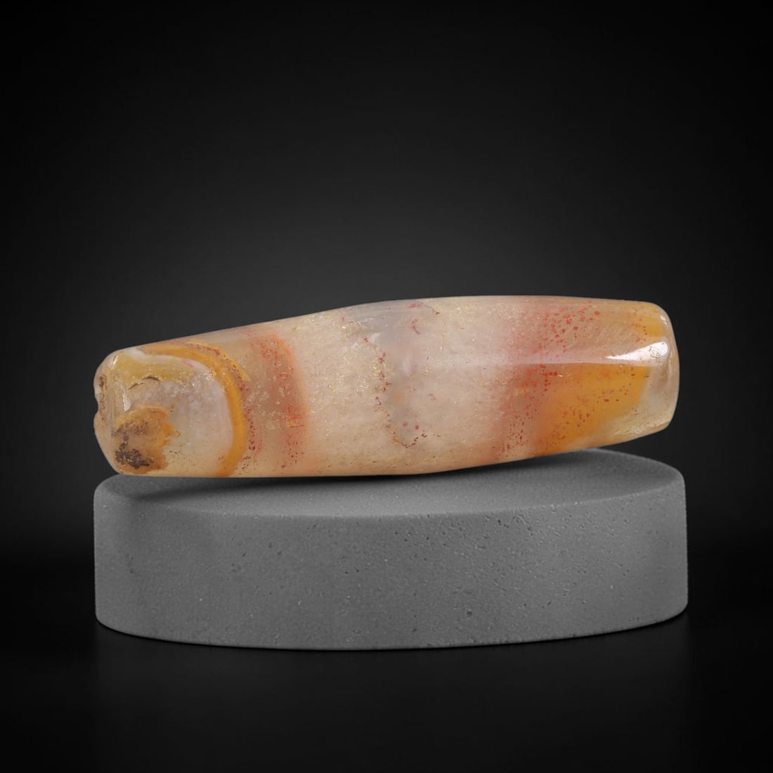 Ancient Banded Agate Bead - Near Eastern Artifact: This artifact is crafted from natural banded agate, shaped into an elongated tapered barrel form with striking concentric banding in warm amber, cream, and soft red hues, accented by scattered red min